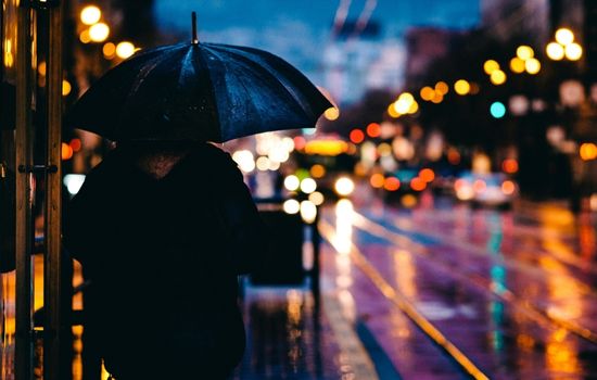 en person som står i mörkret med paraply upplyst av stadsljuset
